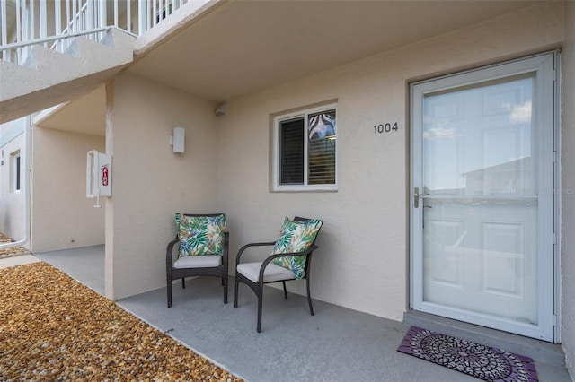view of exterior entry with stucco siding, a balcony, and a patio