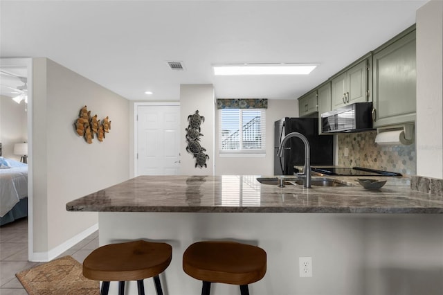 kitchen featuring black appliances, green cabinetry, a peninsula, light tile patterned flooring, and dark stone counters