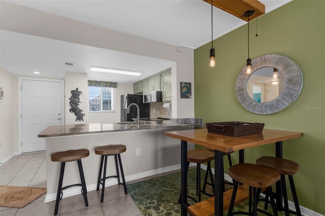 kitchen with a peninsula, a kitchen breakfast bar, light tile patterned flooring, baseboards, and stainless steel microwave