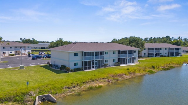 rear view of house with uncovered parking, a water view, and a lawn