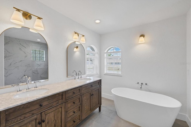 full bath featuring healthy amount of natural light, double vanity, a freestanding tub, baseboards, and recessed lighting