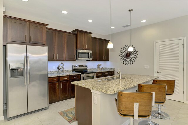 20636 Swallowtail Ct, Venice, FL 34293 - kitchen featuring appliances with stainless steel finishes, a sink, light tile patterned floors, dark brown cabinetry, and light stone counters