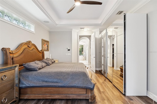 5850 Saddle Oak Trl, Sarasota, FL 34241 - bedroom featuring a tray ceiling, multiple windows, arched walkways, light wood finished floors, and ornamental molding