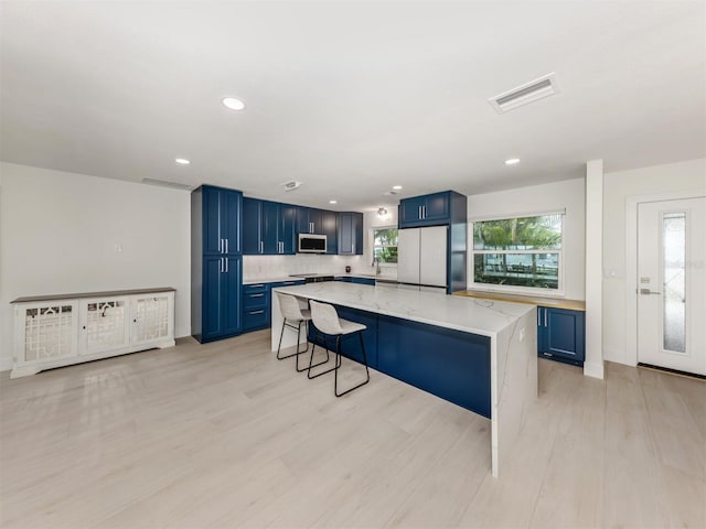832 Whitecap Cir Unit 5, Venice, FL 34285 - kitchen featuring blue cabinetry, stainless steel microwave, freestanding refrigerator, light wood finished floors, and recessed lighting