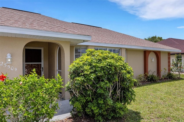 25509 Arequipa Dr, Punta Gorda, FL 33983 - view of exterior entry with stucco siding, roof with shingles, and a lawn