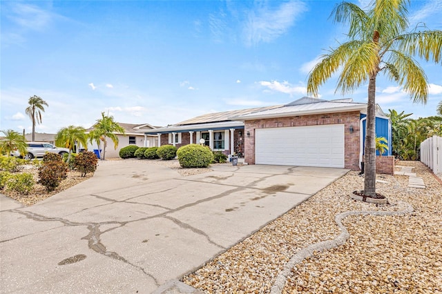ranch-style house with concrete driveway, brick siding, a garage, roof mounted solar panels, and fence