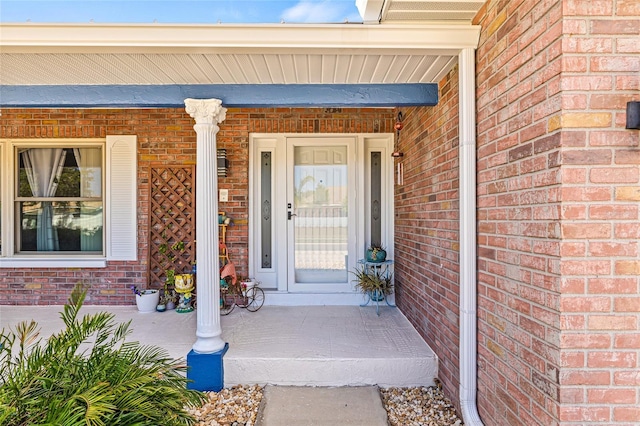 view of exterior entry with a porch and brick siding