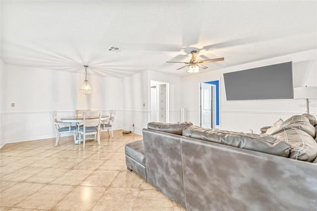 living area featuring ceiling fan, wainscoting, and a textured ceiling