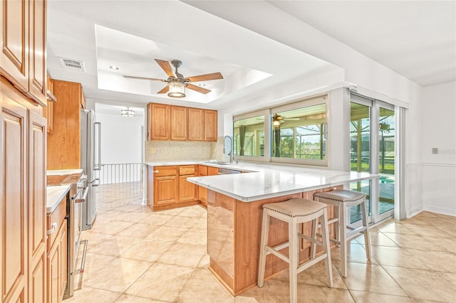 kitchen with appliances with stainless steel finishes, a peninsula, ceiling fan, and a kitchen bar