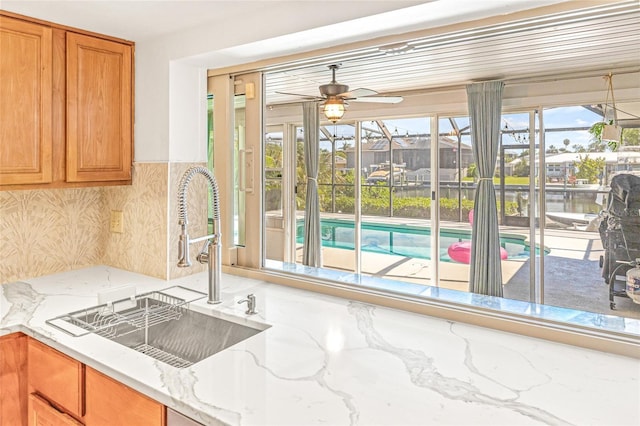 kitchen with a sink, ceiling fan, a sunroom, and light stone counters
