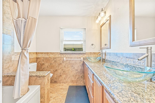 full bathroom featuring tile walls, toilet, double vanity, tile patterned floors, and wainscoting