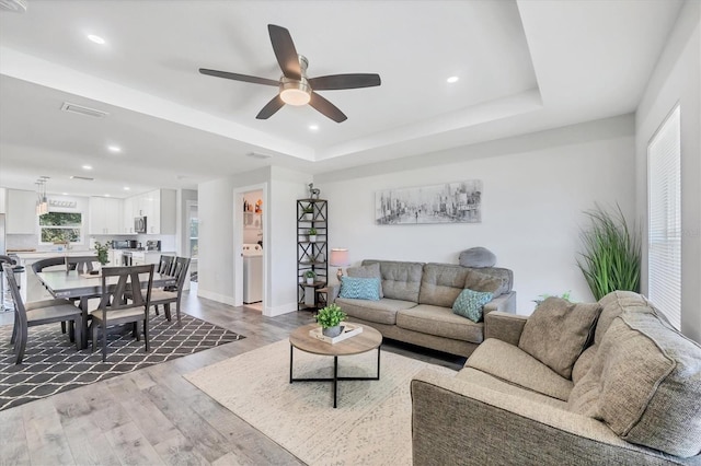 12031 Saragossa Ln, North Port, FL 34287 - living room featuring light wood-type flooring, ceiling fan, recessed lighting, washer / dryer, and a tray ceiling
