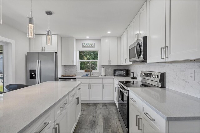 12031 Saragossa Ln, North Port, FL 34287 - kitchen with stainless steel appliances, a sink, wood finished floors, decorative light fixtures, and white cabinets