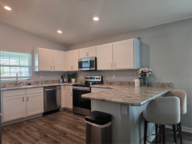 3003 58th Way E, Palmetto, FL 34221 - kitchen featuring appliances with stainless steel finishes, a peninsula, white cabinets, dark wood-style flooring, and a breakfast bar