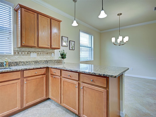kitchen with a peninsula, ornamental molding, brown cabinets, a chandelier, and light stone countertops