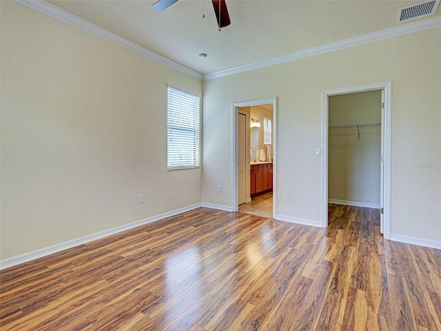 unfurnished bedroom with ornamental molding, wood finished floors, a spacious closet, baseboards, and a closet
