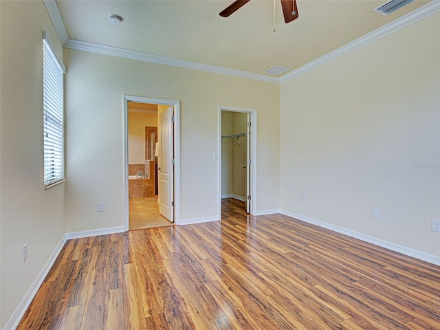 unfurnished bedroom featuring wood finished floors, crown molding, a walk in closet, baseboards, and a closet