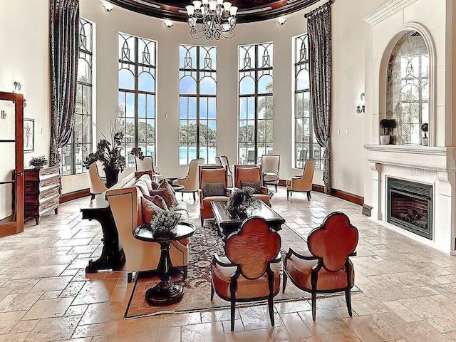 dining space with stone tile flooring, a towering ceiling, a chandelier, baseboards, and a fireplace