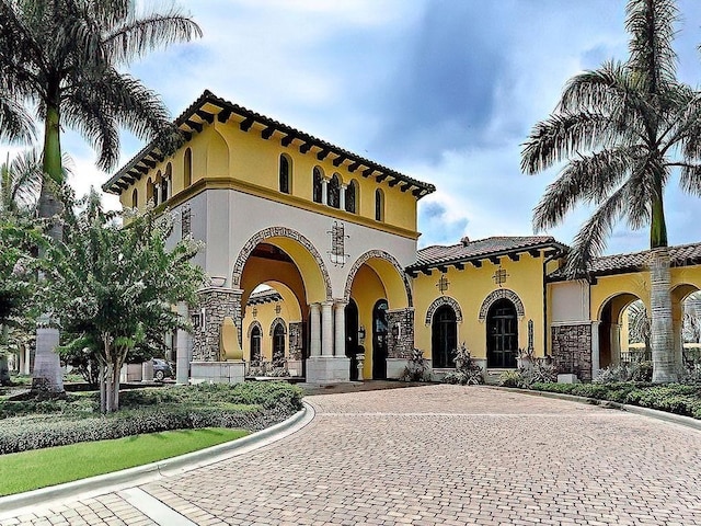 mediterranean / spanish house featuring stucco siding, curved driveway, and stone siding