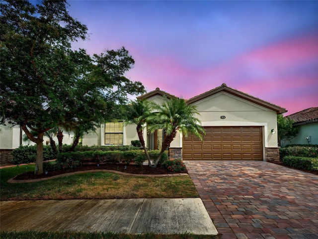 view of front of property featuring stucco siding, an attached garage, decorative driveway, and stone siding