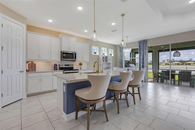 629 Ibiza Loop, Venice, FL 34292 - kitchen with appliances with stainless steel finishes, light tile patterned floors, light countertops, a sink, and a kitchen island with sink