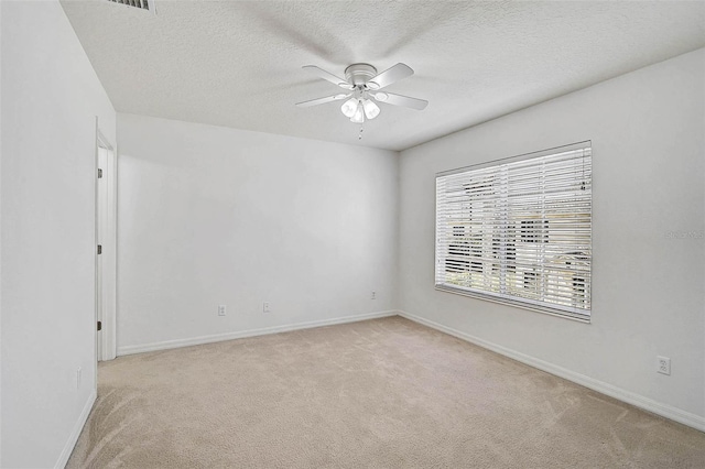 spare room featuring ceiling fan, light colored carpet, baseboards, and a textured ceiling