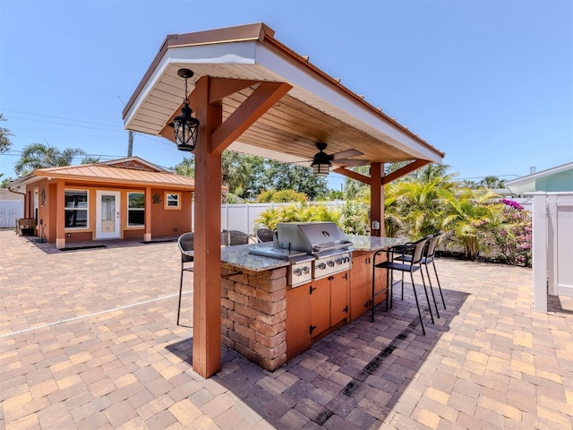 view of patio with an outdoor kitchen, grilling area, ceiling fan, an outdoor bar, and fence