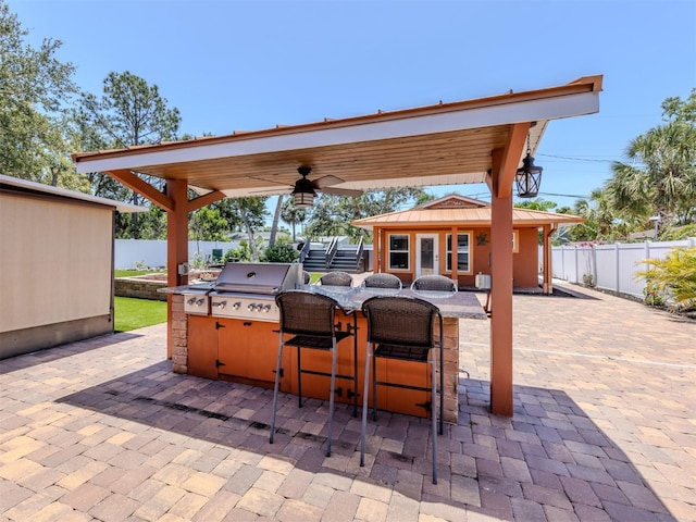 view of patio with a grill, exterior kitchen, fence, an outbuilding, and ceiling fan
