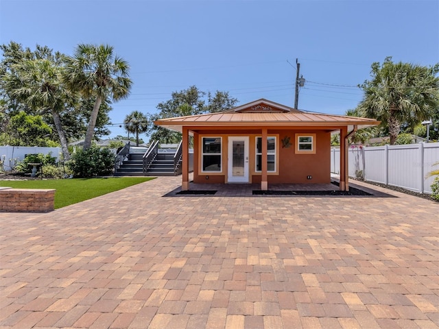 rear view of house with fence, stucco siding, stairs, and a porch