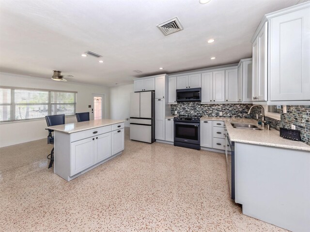 kitchen featuring black range with electric cooktop, a sink, freestanding refrigerator, tasteful backsplash, and a kitchen island