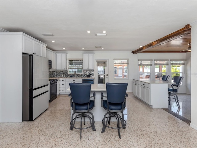 kitchen with fridge, black range oven, a kitchen bar, light countertops, and a kitchen island