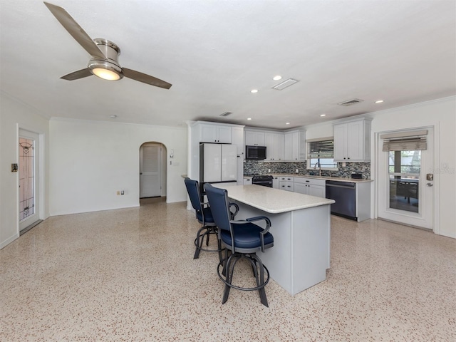 kitchen featuring dishwashing machine, arched walkways, a kitchen bar, light countertops, and a kitchen island