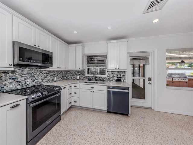 kitchen featuring appliances with stainless steel finishes, a sink, decorative backsplash, white cabinets, and light countertops