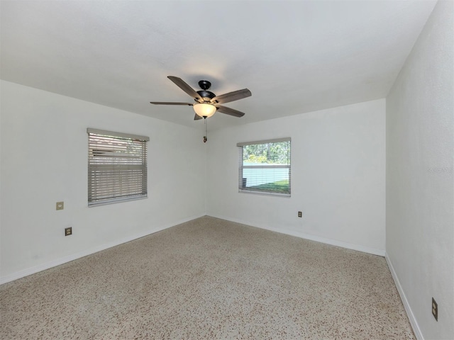 spare room featuring speckled floor, a ceiling fan, and baseboards
