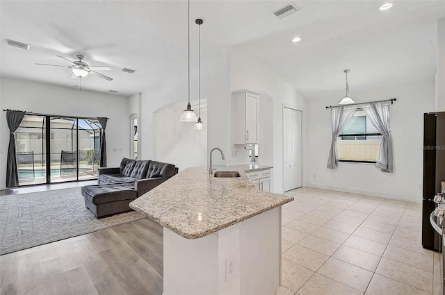 kitchen featuring a sink, ceiling fan, a peninsula, light stone counters, and white cabinets