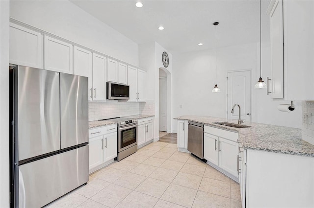 kitchen featuring appliances with stainless steel finishes, a sink, tasteful backsplash, arched walkways, and light tile patterned flooring