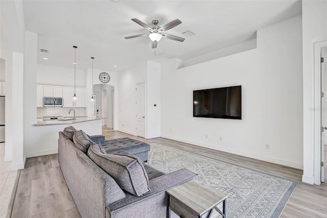 living room with a ceiling fan, light wood-style flooring, and baseboards