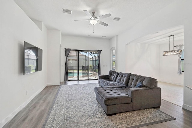 living room featuring wood finished floors, a ceiling fan, baseboards, and arched walkways