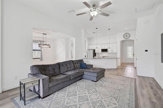 living room featuring light wood-style floors, a ceiling fan, arched walkways, and baseboards