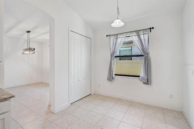 unfurnished dining area featuring light tile patterned floors, baseboards, and arched walkways