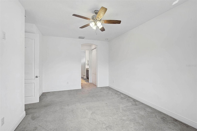 carpeted spare room with arched walkways, ceiling fan, and baseboards