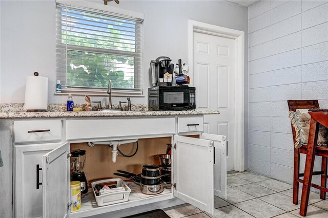 422 Polk Ave, Cape Canaveral, FL 32920 - kitchen with black microwave, a sink, white cabinets, light tile patterned flooring, and light stone countertops