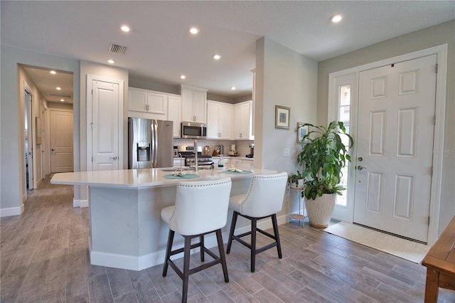 10410 Inglenook Ter, Palmetto, FL 34221 - kitchen with appliances with stainless steel finishes, wood finished floors, a kitchen bar, white cabinets, and tasteful backsplash