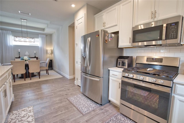 10410 Inglenook Ter, Palmetto, FL 34221 - kitchen featuring appliances with stainless steel finishes, light wood finished floors, white cabinets, tasteful backsplash, and light countertops