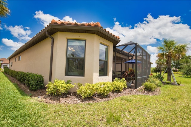 10410 Inglenook Ter, Palmetto, FL 34221 - view of home's exterior with a tiled roof, stucco siding, a yard, and glass enclosure