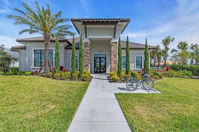 10410 Inglenook Ter, Palmetto, FL 34221 - view of front of house with stucco siding, a tiled roof, a front lawn, french doors, and stone siding
