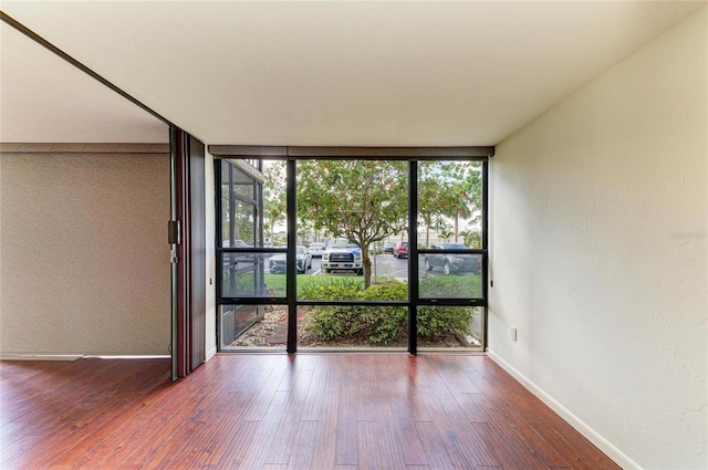 618 Bird Bay Dr S Unit 110, Venice, FL 34285 - spare room featuring a wall of windows, baseboards, wood finished floors, and a textured wall