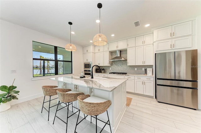 12816 Morning Mist Pl, Venice, FL 34293 - kitchen with stainless steel appliances, wall chimney range hood, decorative backsplash, a kitchen island with sink, and light stone counters