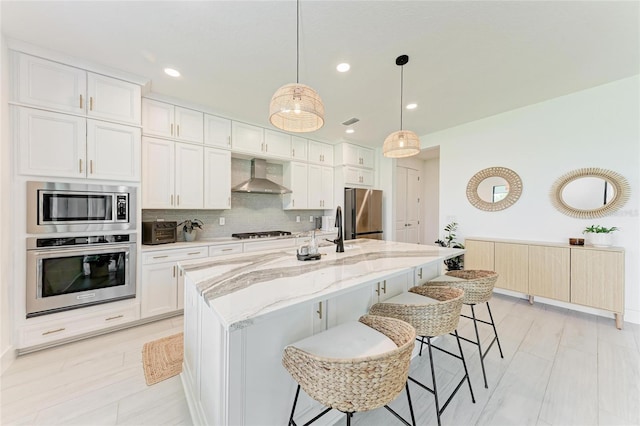 12816 Morning Mist Pl, Venice, FL 34293 - kitchen with appliances with stainless steel finishes, wall chimney exhaust hood, white cabinets, an island with sink, and decorative backsplash