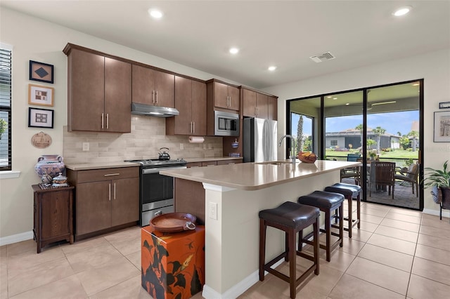13486 Nobilio St, Venice, FL 34293 - kitchen featuring stainless steel appliances, under cabinet range hood, light countertops, backsplash, and an island with sink